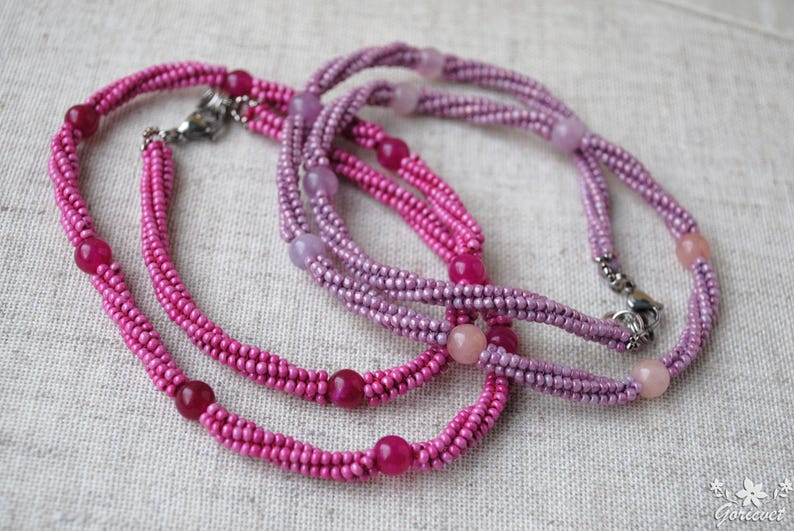 Puede incluir: Dos collares de cuentas, uno rosa y otro morado, con cuentas de piedras preciosas m&aacute;s grandes intercaladas.