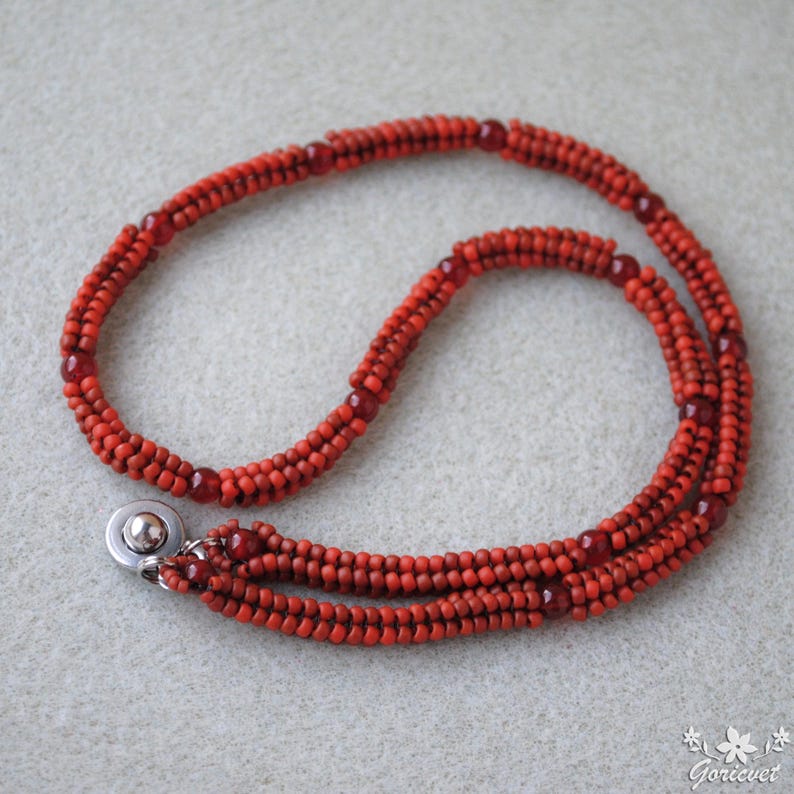 May include: A handmade necklace featuring a vibrant red beaded design. The necklace is composed of small, tightly woven beads, with larger, darker red beads interspersed throughout. A silver-colored clasp secures the necklace.