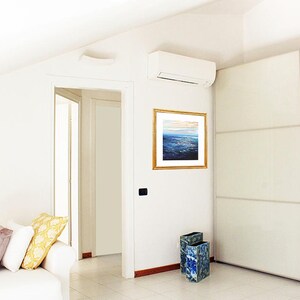 May include: A white room with a white couch, a white door, a white closet, and a white air conditioner. There is a framed painting of a seascape on the wall. There are two blue and green decorative vases on the floor.