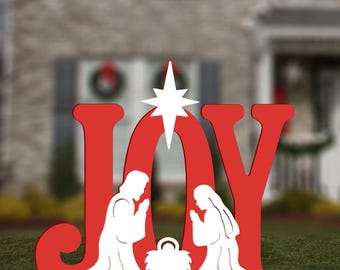 May include: A red outdoor Christmas decoration spelling "JOY" with a white star and nativity scene. The letters are large and stand on a grassy lawn. The nativity scene includes figures of Mary, Joseph, and baby Jesus in a manger.