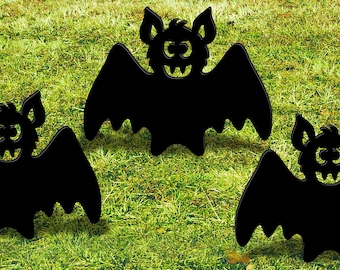 Puede incluir: Tres siluetas negras recortadas de murciélagos con una cara de dibujos animados amigable. Los murciélagos están dispuestos en una fila sobre un césped verde.