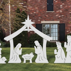 May include: White wooden nativity scene with a star on top of the stable. The figures include Mary, Joseph, baby Jesus, a shepherd, three wise men, and an angel. The scene is set up on a green lawn in front of a brick house.