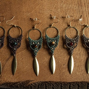 May include: Six pairs of handmade earrings with a macrame design. Each pair features a different gemstone in the centre, including green, brown, and red. The earrings have a gold-coloured leaf-shaped pendant.