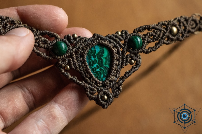 May include: A brown macrame necklace with a green malachite stone pendant and two smaller green malachite stones on the sides.