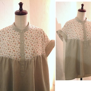 Könnte beinhalten: Ein beige-weißes Baumwollkleid mit einem floralen Oberteil und einem unifarbenen Unterteil. Das Kleid hat einen Knopfleisten vorne und kurze Ärmel.