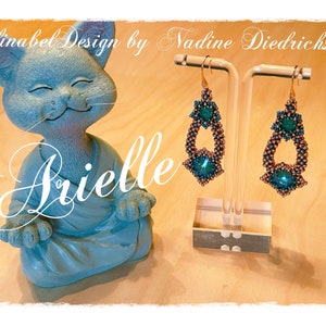 Könnte beinhalten: Ein Paar türkisfarbene und kupferfarbene Perlenohrringe in Tropfenform mit einem Kristall-Akzent. Die Ohrringe werden auf einem Ständer präsentiert.