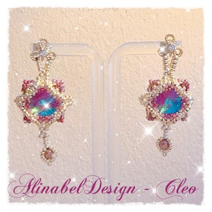 Könnte beinhalten: Ein Paar rosafarbene und goldene Perlenohrringe mit einem großen, schillernden Kristall in der Mitte. Die Ohrringe hängen an einem durchsichtigen Ständer. Der Text "Alinabe Design - Cleo" ist am unteren Rand des Bildes sichtbar.