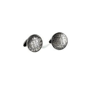 May include: A pair of silver cufflinks with a circular design featuring a pattern of symbols and letters.