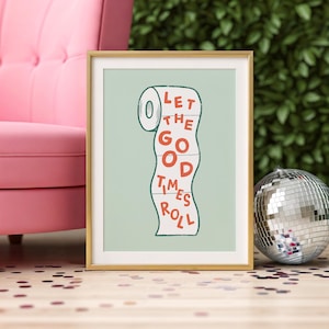 May include: A framed art print with a gold frame. The print features a stylized illustration of a roll of toilet paper with the words "LET THE GOOD TIMES ROLL" in red letters. The background is a light green color.