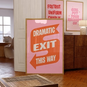May include: A framed pink poster with the words "DRAMATIC EXIT THIS WAY" in white and orange. Two other framed posters are visible, one with the words "FOXTROT UNIFORM CHARLIE" and another with "GIRL PUT YOUR RECORDS ON".