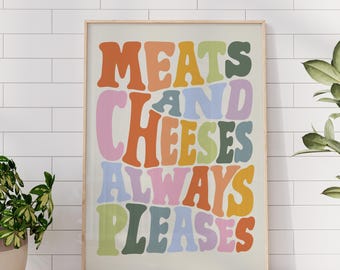 May include: A framed print with the words "MEATS AND CHEESES ALWAYS PLEASES" in a retro font. The text is in various colors, including orange, pink, green, and blue, against a cream background. The frame is a light wood color.