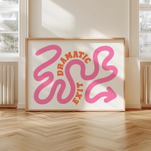 May include: A framed print featuring the words "DRAMATIC EXIT" in pink and orange. The pink text is in a flowing, curvy design with an arrow. The artwork is displayed on a light wall in a room with windows and radiators.