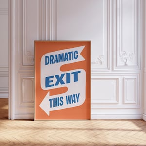 May include: A framed poster with the words "DRAMATIC EXIT THIS WAY" in blue and white on an orange background. The poster is in a room with white paneling and a wooden floor.