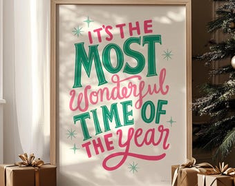 May include: A framed print with the text "IT'S THE MOST Wonderful TIME OF THE Year" in green and pink. The print is in a light wood frame, with wrapped gifts and a Christmas tree in the background.