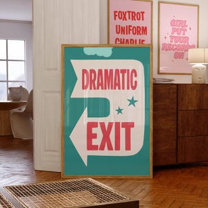 Puede incluir: Un póster enmarcado con las palabras "DRAMATIC EXIT" en letras rojas sobre un fondo turquesa. La flecha blanca apunta hacia la izquierda. En el fondo se ven otros dos pósteres enmarcados, uno con las palabras "FOXTROT UNIFORM CHARLIE".