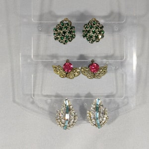 May include: Three pairs of vintage clip-on earrings. The first pair is green, the second pair is pink, and the third pair is blue.
