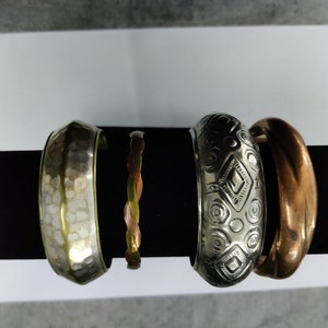 May include: Four metal bangles, one with a hammered finish, one with a braided design, one with a geometric pattern, and one with a smooth, copper finish.