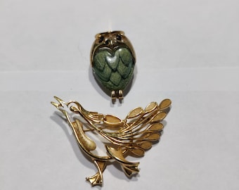 May include: Two gold-toned brooches, one shaped like an owl with green enamel and the other shaped like a bird with a spread tail.