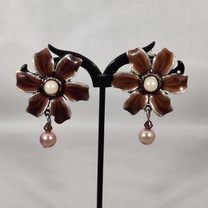 Può includere: Un paio di orecchini pendenti a forma di fiore marroni con un centro di perla e una goccia di perla rosa.