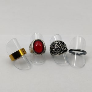 Op de afbeelding: Vier ringen op displaystandaards. Eén ring is goud, één heeft een rode steen, één heeft een zilveren vrijmetselaars symbool en één is een gladde zilveren band.