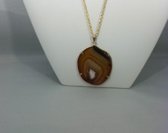May include: A gold chain necklace with a brown agate pendant. The pendant is a slice of agate with a natural pattern of brown and white.