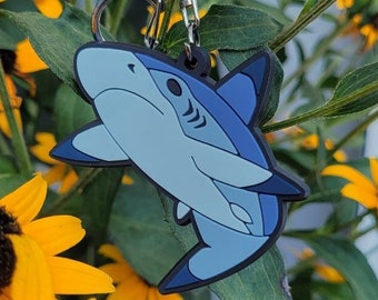 May include: A blue and gray shark keychain with a black key ring hanging from a yellow flower.
