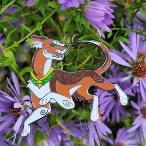 May include: An enamel pin featuring a cartoon dog in brown and white with green eyes and a green and gold collar. The pin is displayed against a backdrop of purple flowers.