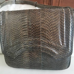 Peut inclure: Un sac à bandoulière en peau de serpent brun foncé avec une fermeture à rabat. Le sac a une surface texturée et un léger brillant.