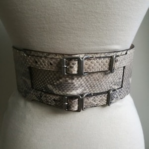Peut inclure: Une ceinture à double boucle en peau de serpent brun clair avec des boucles argentées.