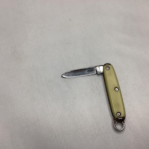 May include: A small, vintage folding knife with a cream-colored handle and a stainless steel blade. The blade is partially open, revealing the sharp edge. The handle has three rivets and a metal ring at the base. The knife is marked "USA".