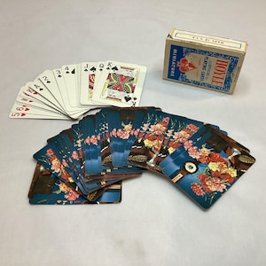 May include: A collection of playing cards, including a deck of miniature Hoyle playing cards and two fanned-out sets of cards. One set features standard card faces, while the other has a floral design on a blue background.