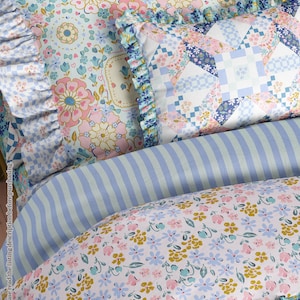May include: Close-up of a bed with floral and geometric patterned bedding. The pillows and duvet feature a mix of pink, blue, and yellow floral designs, along with a blue and white checkered pattern. The bedding has a ruffled edge.