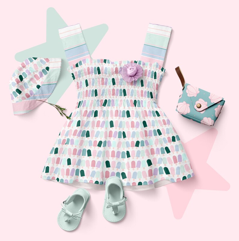 May include: A white dress with a pink, green, and blue popsicle pattern. The dress has a ruffled neckline and thin straps. The dress is paired with a matching hat, a small purse, and a pair of light blue sandals.