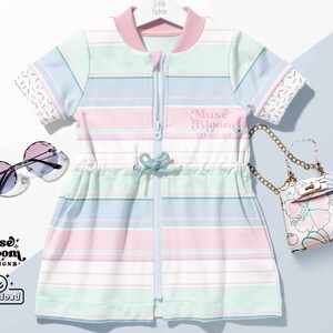 May include: A pink and blue striped dress with short sleeves and a zipper down the front. The dress has a drawstring waist and a small white bag with floral print is in the background.