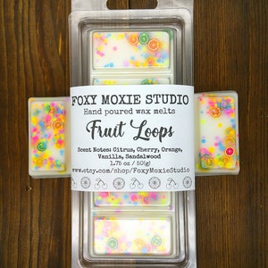 May include: A clear plastic container with three wax melts. The wax melts are white with colorful sprinkles and fruit slices. The label reads "FOXY MOXIE STUDIO Hand poured wax melts Fruit Loops Scent Notes: Citrus, Cherry, Orange, Vanilla, Sandalwood 1.75 oz/50(g) www.etsy.com/shop/FoxyMoxieStudio"