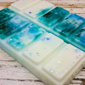 K&ouml;nnte beinhalten: Ein Wachsschmelzblock mit einem blauen und wei&szlig;en Marmormuster und schimmerndem Glitzer. Der Block ist in sechs Quadrate unterteilt.