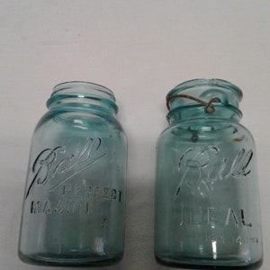 May include: Two vintage blue glass Ball mason jars with metal lids. The jar on the left says "Ball Perfect Mason" and the jar on the right says "Ball Ideal".