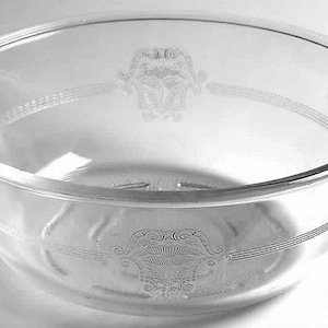 May include: Clear glass serving bowl with etched decorative patterns. The bowl has a rounded shape with two small handles and a wide rim. The etched design includes floral and geometric elements.