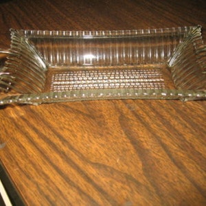 May include: A clear glass serving dish with ribbed sides and a textured bottom. The dish has two handles on the sides.
