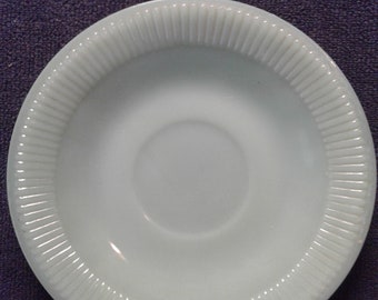 May include: A white, ribbed, saucer for a teacup. The saucer is made of milk glass and has a slightly scalloped edge.