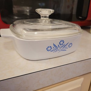 May include: White casserole dish with a glass lid and a blue floral design. The design features blue flowers and leaves on a white background.