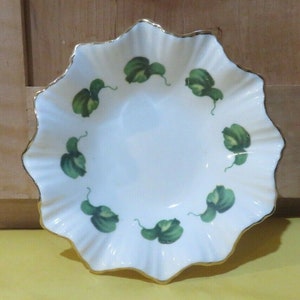 May include: A white porcelain bowl with a scalloped edge and a gold rim. The bowl is decorated with a green leaf pattern.