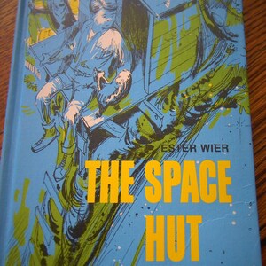 May include: A blue book cover with a yellow and green illustration of a person in a space hut. The title of the book is "The Space Hut" by Ester Wier, illustrated by Leo Summers.