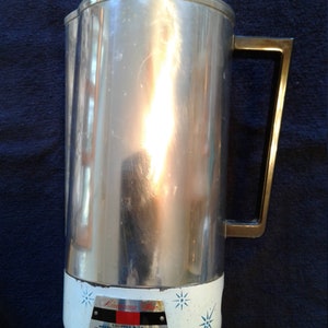 May include: A silver and white coffee maker with a black handle. The coffee maker has a starburst design and the text "Lumarama Star" and "Equipped with Westinghouse Thermostat" on the front.