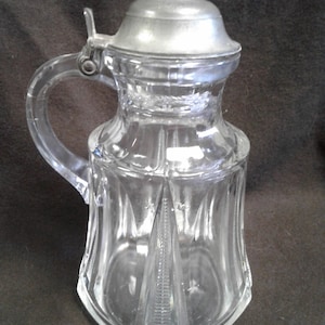 May include: A clear glass pitcher with a pewter lid and a handle. The pitcher has a textured, diamond-shaped pattern.