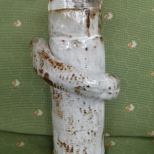 May include: A white ceramic vase with brown glaze accents. The vase has a unique, twisted design and a wide opening.