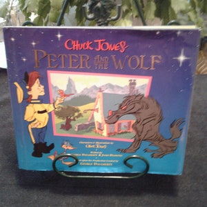May include: A purple book with a yellow spine titled "Chuck Jones and the Peter Wolf". The cover features a cartoon illustration of a boy in a yellow jacket and a wolf.