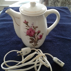 May include: White porcelain electric teapot with a floral design and a gold trim. The teapot has a cord with a plug that says "JAPAN".
