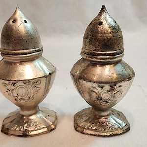 May include: A pair of silver salt and pepper shakers with ornate designs and a domed top.