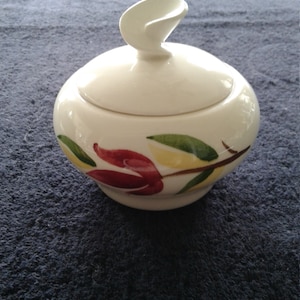 May include: White ceramic sugar bowl with a floral design featuring red, yellow, and green leaves. The lid has a unique curved design.